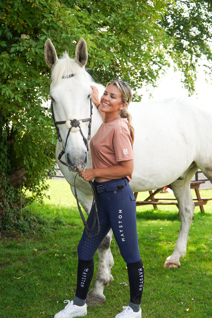 Woman in equestrian attire standing next to a white horse in a grassy area with trees.
luxury quality pink blush t shirt and fabric is specially crafted for active duty, providing flexibility and ease of movement for any busy lifestyle. An ideal choice for a day at the yard, in the saddle, or during your grooming duties, its loose-fitting design guarantees complete freedom. high gloss silicone branding