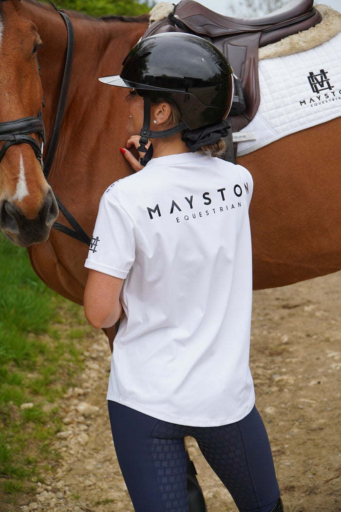 Person riding a horse wearing a white shirt with 'Mayston' branding. white luxury quality t shirt and fabric is specially crafted for active duty, providing flexibility and ease of movement for any busy lifestyle. An ideal choice for a day at the yard, in the saddle, or during your grooming duties, its loose-fitting design guarantees complete freedom. high gloss black silicone branding