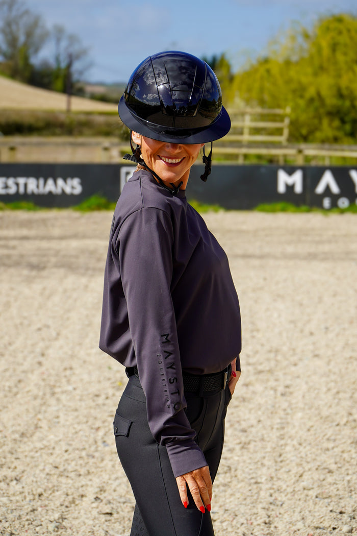 Person wearing a dark helmet and purple long-sleeve shirt in an equestrian setting. grey long sleeve durlston sports technical top in buttery-soft nylon sports fabric, this top delivers unbeatable comfort with a sleek, performance feel. From breezy dog walks to competition days, it’s designed to move with you. high gloss silicone branding. thumb holes