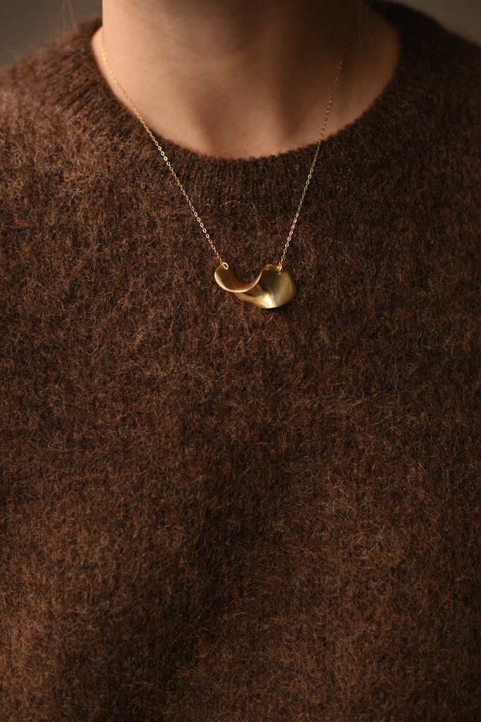 Gold wave brass pendant necklace on model's collar with chain and clasp