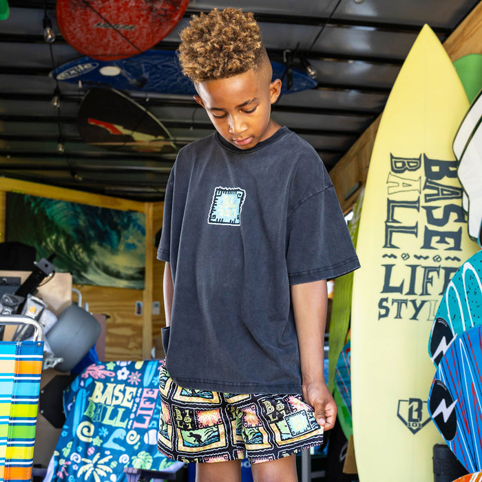Youth model wearing multi-color youth shorts with "Wave Goodbye" design