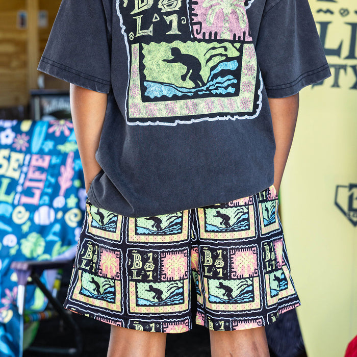 Youth model wearing multi-color youth shorts with "Wave Goodbye" design