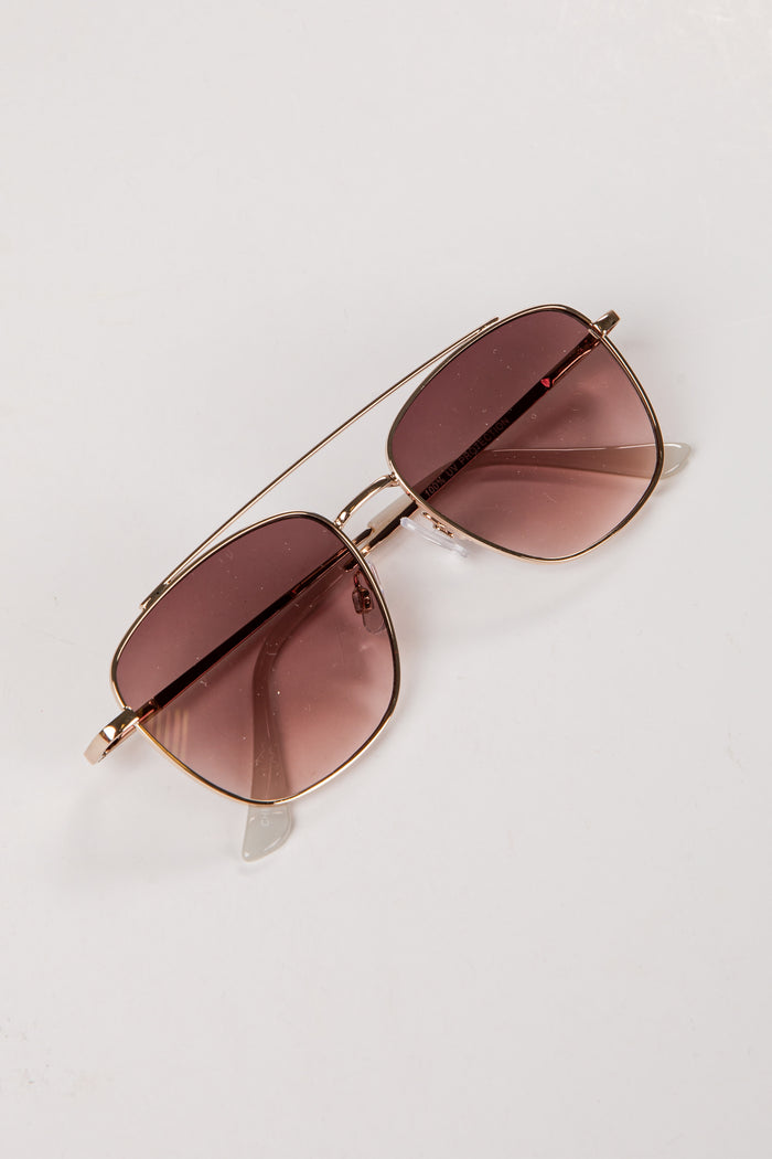Sunglasses with brown lenses and gold frame on a light gray background