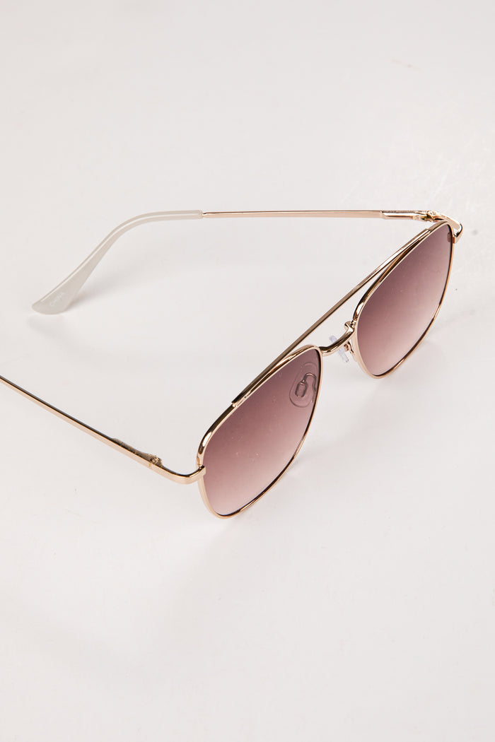 Gold-framed sunglasses with pink-tinted lenses on a light gray background