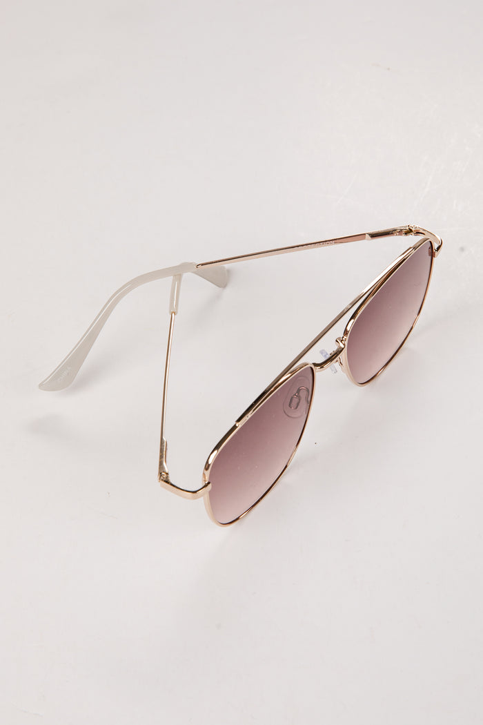Sunglasses with gold frame and pink lenses on a light gray background