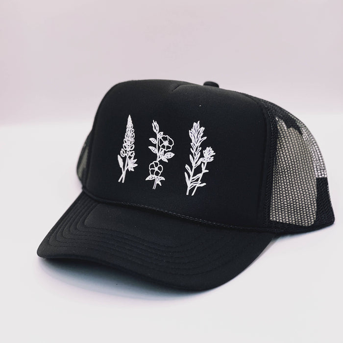 Black Wildflowers adult trucker hat by Made of Mountains featuring a floral embroidered design and adjustable mesh back.