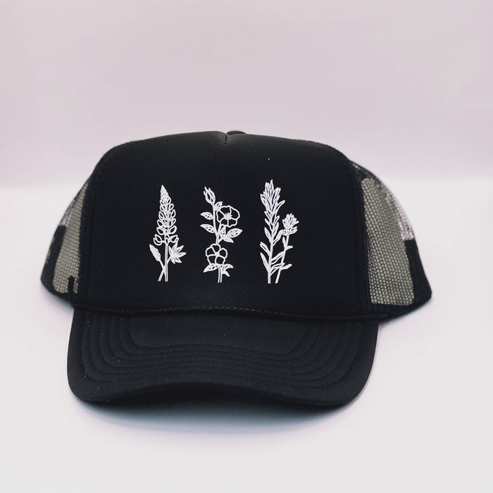 Black Wildflowers adult trucker hat by Made of Mountains with floral embroidery and mesh back, casual outdoor accessory.